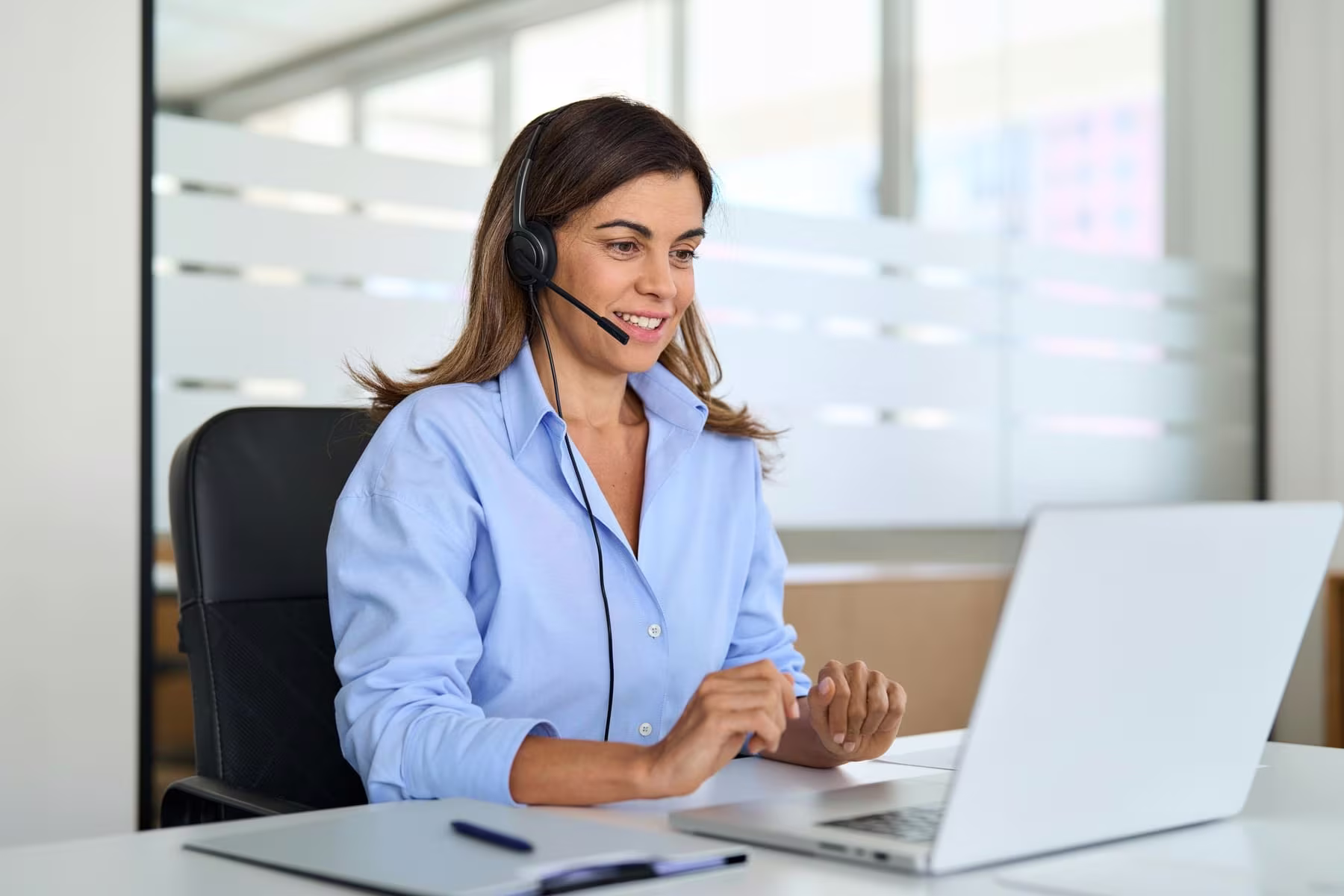 Smiling customer support agent with a headset at a laptop