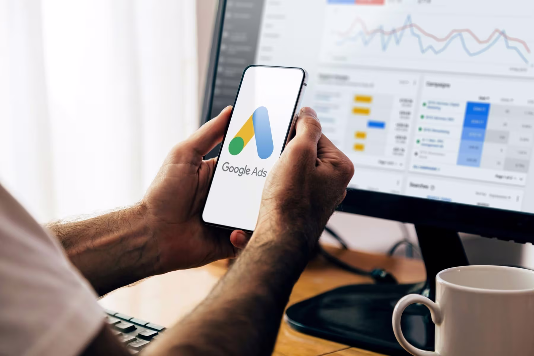 Google Ads app on a smartphone at a desk with a campaign report on screen